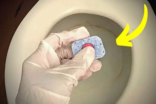 Une personne tenant une tablette de lave vaisselle au dessus des toilettes 