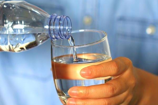 Une personne qui verse de l'eau en bouteille dans un verre comme remède contre la perlèche