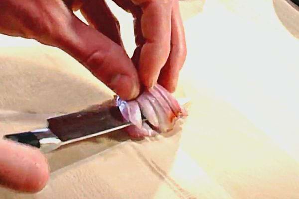 Une personne qui tient du bouts des doigts une échalote pour la découper