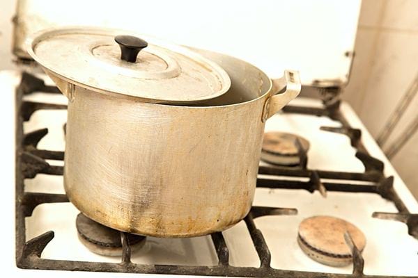 Une casserole avec son couvercle en aluminium qui est sale sur une plaque de gaz