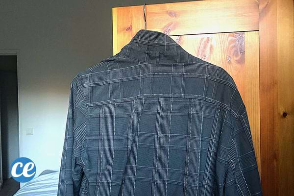 Une chemise à carreaux grise sur un cintre qui est suspendue sur la porte d'une armoire 