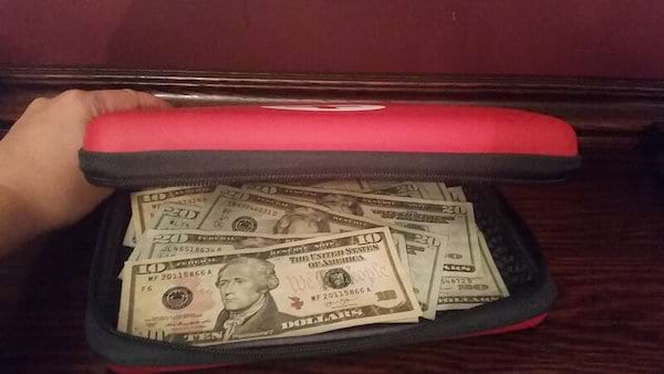 Une personne qui tient une trousse de secours d'urgence rouge avec pleins de dollars dedans 