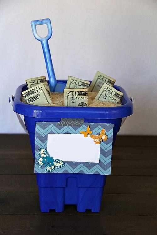 Plusieurs dollars qui sont dans un seau de plage bleu avec du sable 