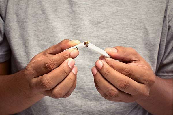 Un homme avec un tee-shirt gris qui tient une cigarette cassée