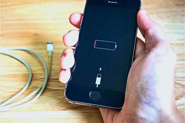 Uma pessoa segurando um iPhone sem carga com o cabo da Apple próximo a ele