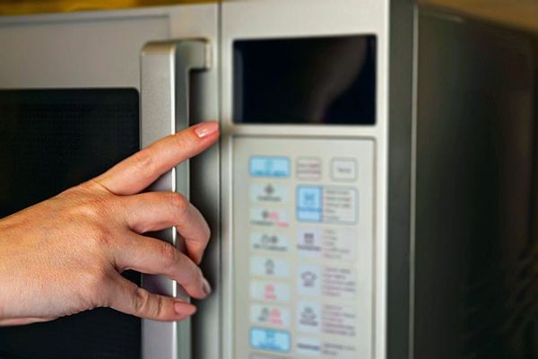 Une femme qui va appuyer sur un micro-ondes