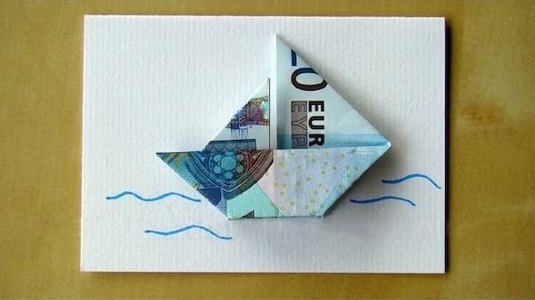 Un billet de 20 euros en origami en forme de bateau sur une feuille avec dessin 