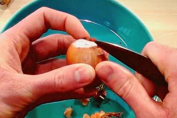 Une personne enlevant la peau d'une échalote à l'aide d'un couteau