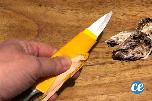 Une personne tenant un couteau jaune avec quelques huîtres juste à côté