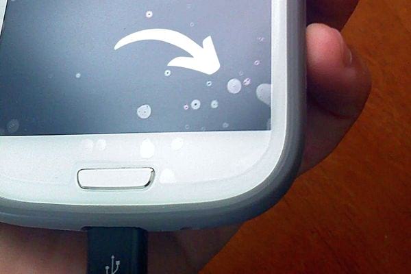 Plusieurs petites bulles sur l'écran de verre trempé d'un smartphone blanc qui est branché