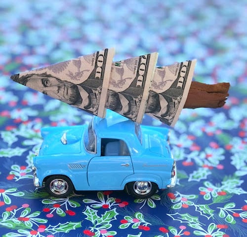 Un petit sapin en origami fait avec des billets Américains sur une petite voiture de collection bleue