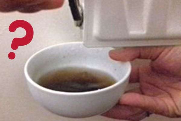 Une personne tenant une tasse à café sous un radiateur avec de l'eau sale à évacuer 