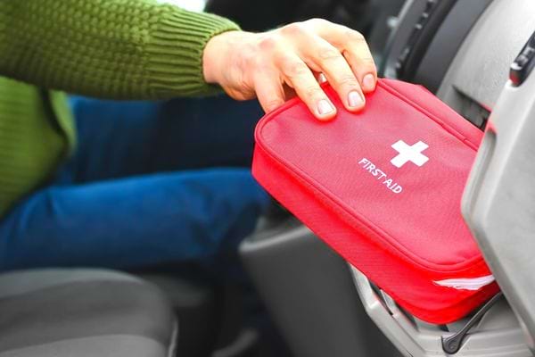 Eine Person legt einen roten Erste-Hilfe-Kasten in ihr Handschuhfach