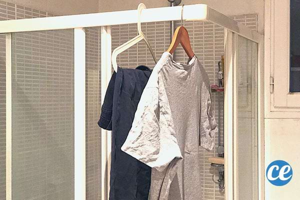Deux vêtements qui sont étendues avec des cintres sur une barre de cabine de douche 