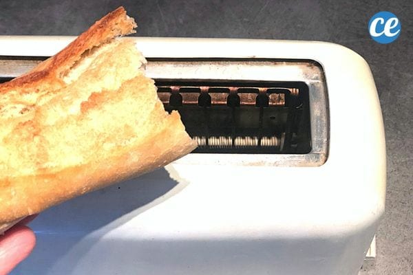 A person holding a piece of baguette over a toaster