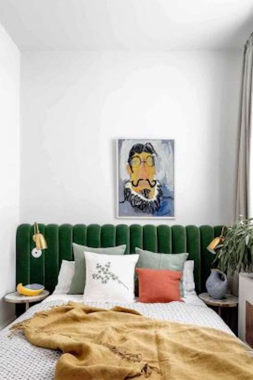Un lit avec une banquette verte en velours en tête de lit