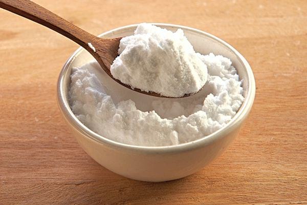 Un petit bol blanc avec une cuillère en bois remplie de bicarbonate de soude 