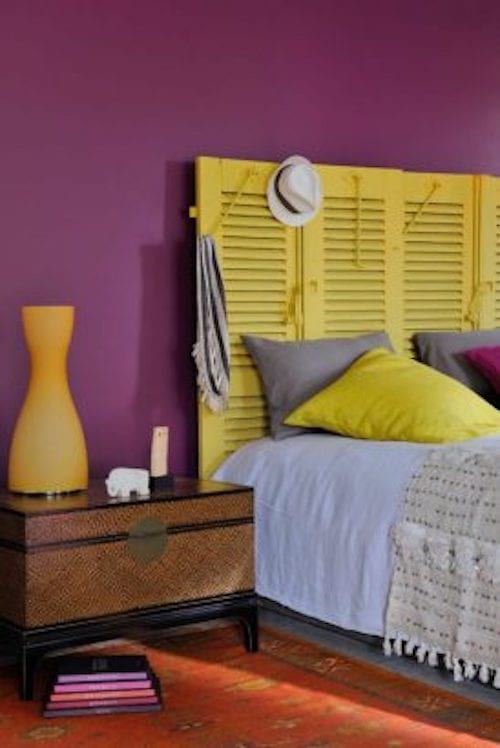 Une chambre violette avec des volets jaunes en tête de lit