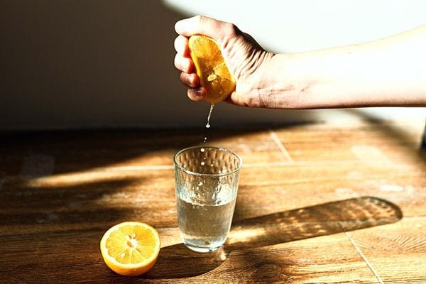 Une personne qui presse un citron découpé dans un verre avec de l'eau