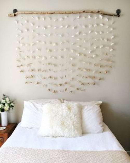 Une tête de lit créée à l'aide de bois et de guirlandes de papier blanc avec des coquillages suspendues