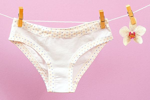 Une culotte en coton accrochée à des pinces à linge sur un fond rose