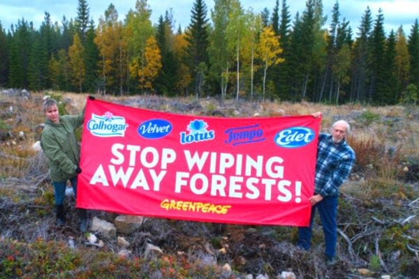 Deux hommes tenant une grosse pancarte rouge devant une forêt