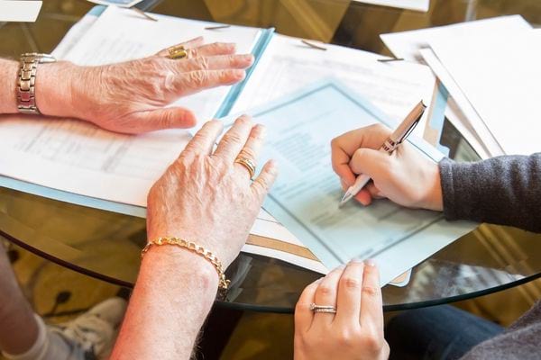 Deux personnes rédigeant sur plusieurs feuilles posées sur une table  