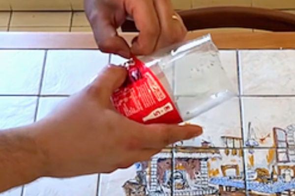 Une personne enlevant l'étiquette rouge sur une bouteille de coca