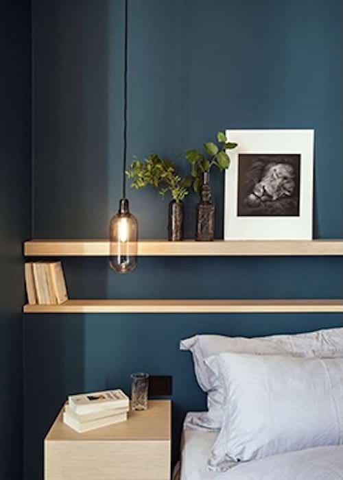 Une grande étagère en bois accrochée derrière un lit avec une lampe suspendue au dessus