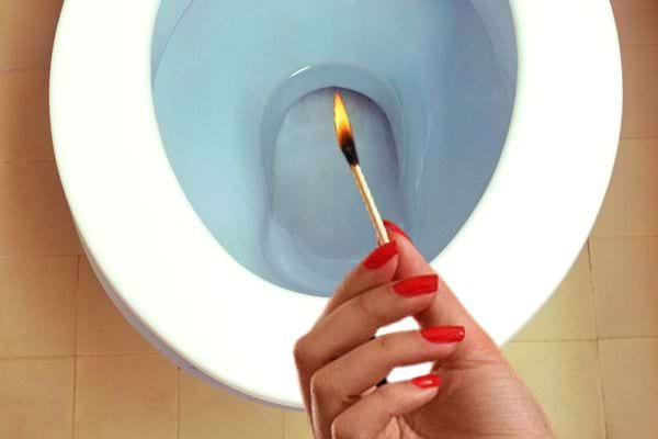 Die Hand einer Frau mit roter Politur hält ein Streichholz über der Toilette