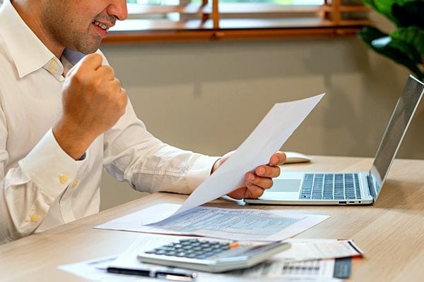 Un homme en chemise blanche tenant une feuille avec un air joyeux 