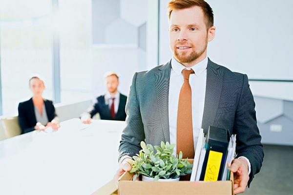 Un homme en costard qui tient un carton avec des affaires avec d'autres personnes derrière