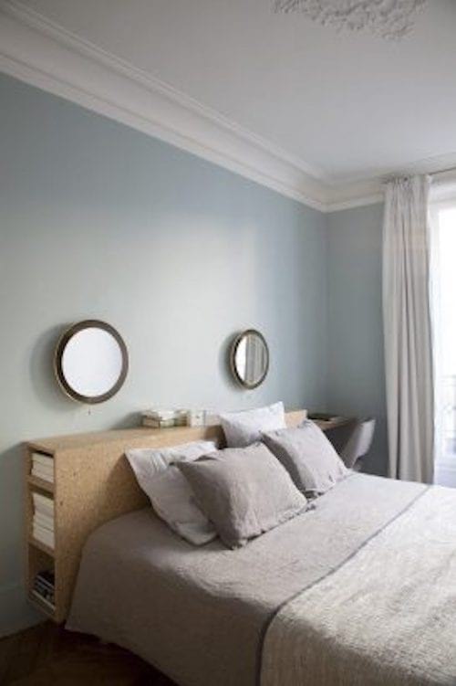 Une chambre avec deux petits miroirs ronds collés au mur avec un meuble en lège en tête de lit