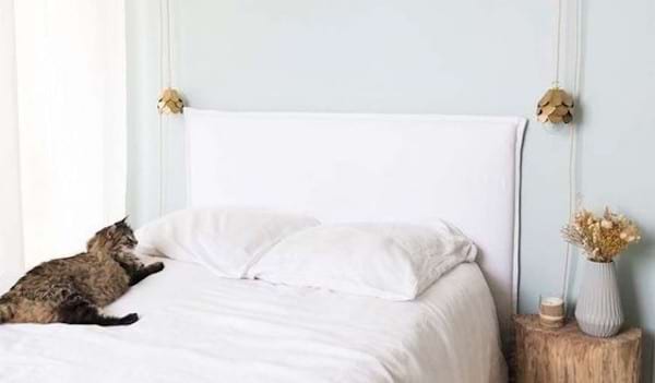 Un lit blanc sur lequel il y a un chat avec une énorme tête de lit en forme d'oreiller