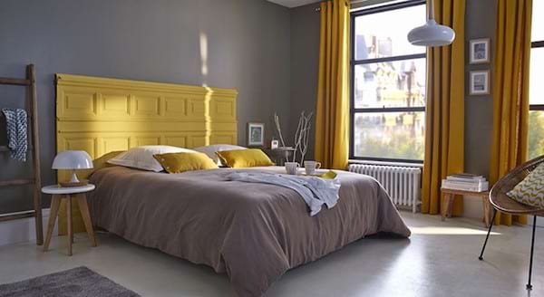 Une chambre en jaune et gris avec un lit et une tête de lit en tissu gris et un coussin jaune
