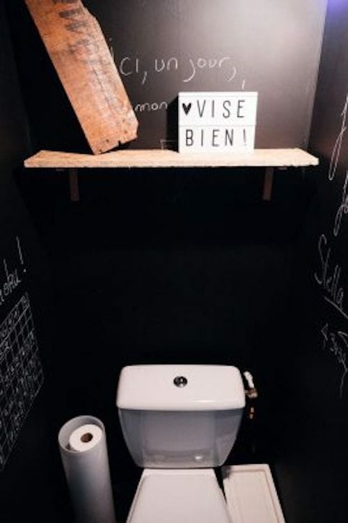 A toilet with a dark style and a pretty funny message on the shelf