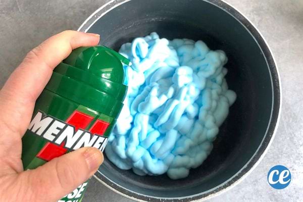 Une personne ayant un tube de mousse à raser verte avec de la mousse bleue dans un seau