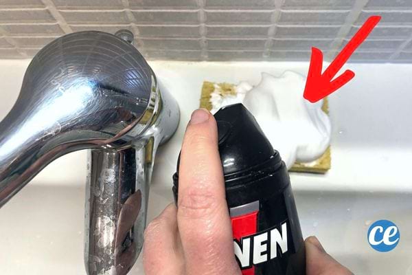 Une personne mettant de la mousse à raser blanche sur une éponge à côté d'un robinet
