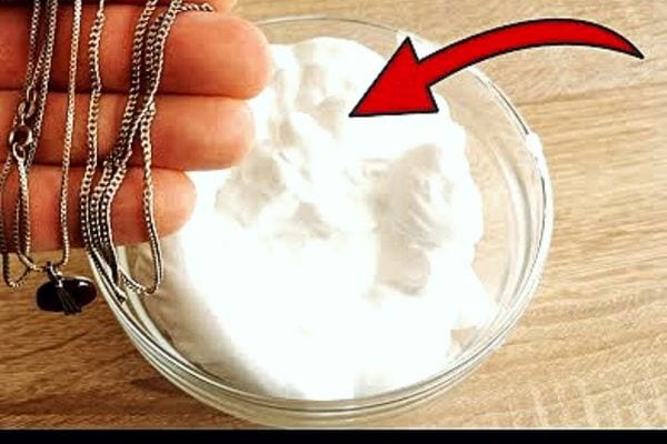 Une personne tenant des bijoux dans sa main au dessus d'un récipient remplie de mousse à raser