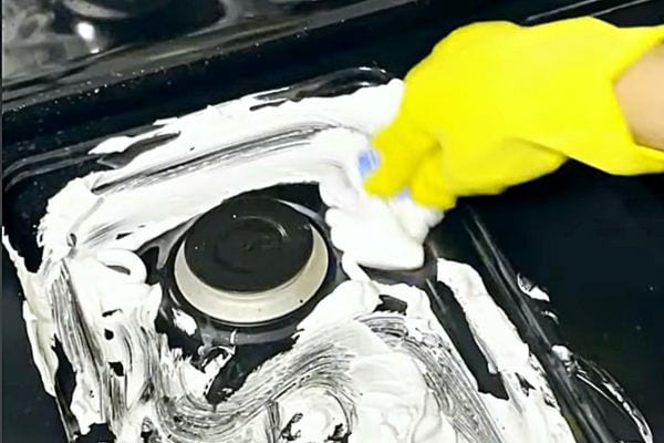 Une personne équipée de gant jaune nettoyant sa plaque de cuisson avec de la mousse à raser 