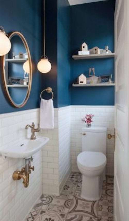 A blue wall with white tiles just below in a toilet 