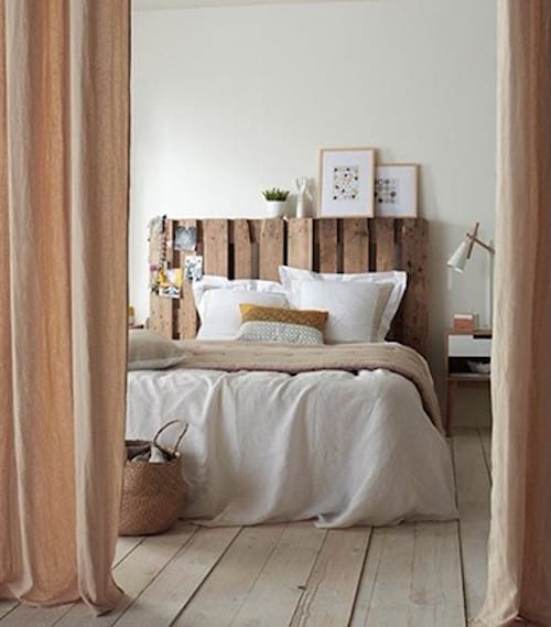 Une chambre beige avec une palette en bois qui est en tête de lit