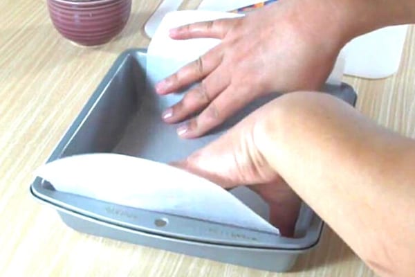 personne qui met du papier cuisson dans un moule à gateau