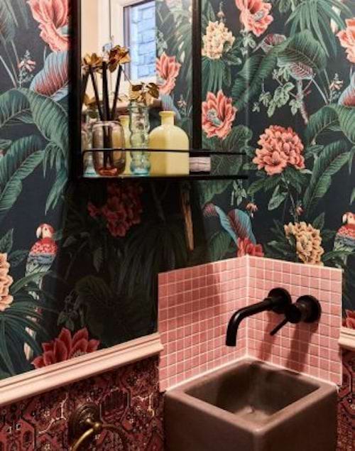 A wallpaper in a jungle style with lots of flowers in a toilet with a small sink