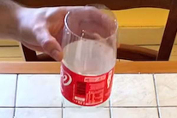 Une personne tenant une bouteille de coca découpée en forme de cylindre