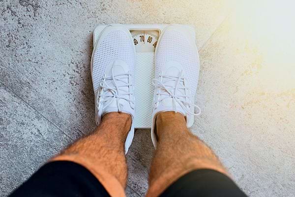Un homme sur un pèse personne avec des baskets blanche