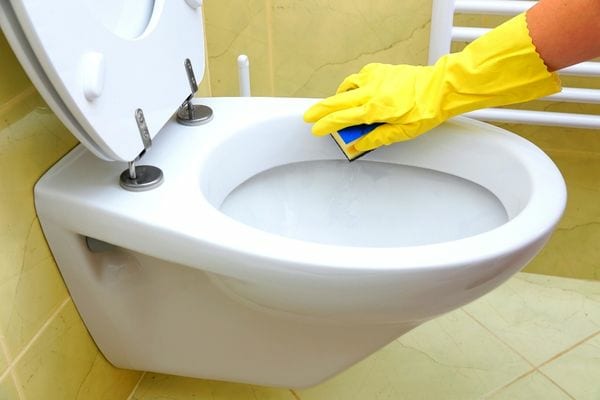 Eine Person reinigt die Toilettenschüssel mit einem gelben Handschuh