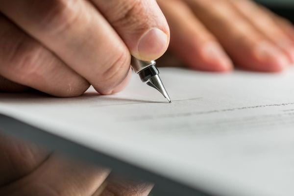 Une personne tenant un stylo plume dans sa main et qui écrit sur une feuille 