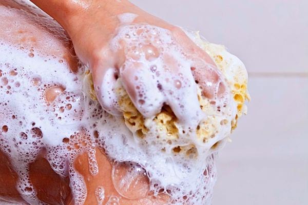 Une personne se nettoyant avec une éponge avec pleins de mousse sur son corps