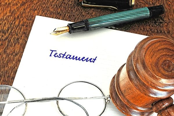 Une feuille où il y a marqué "testament" avec un stylo plume dessus et une paire de lunette